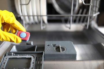 Gloved hands holding dishwasher washing tablet