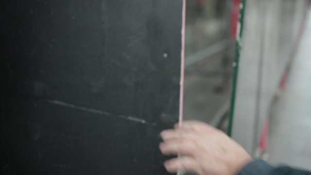Men's Hands In Construction Gloves Hammer A Nail Into The Fence, There Is Dust. Close Up