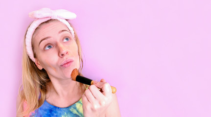 Portrait of beautiful young woman with makeup brush on pink background. Copy space