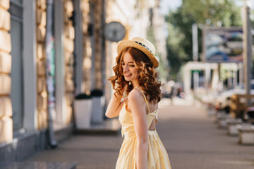 Shapely young woman in yellow dress posing with pleasure in city. Outdoor photo of stunning girl in...