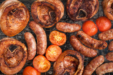 large shank steaks with pork sausages and tomato halves are grilled on a charcoal grill. advertisement of a summer street cafe. family picnic concept. top view