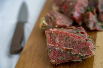 Raw meet slices are laying on wooden cutting board near knife