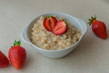 Oatmeal with strawberries in a white bowl. Healthy breakfast with oatmeal and fresh organic berries. Hot and healthy breakfast. Dietary nutrition. Top view, close up