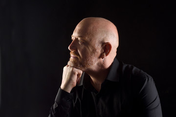portrait of a man in low key, smiling and looking side with  hand on chin