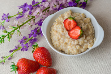 Oatmeal with strawberries in a white bowl. Healthy breakfast with oatmeal and fresh organic berries. Hot and healthy breakfast. Dietary nutrition. Top view, close up
