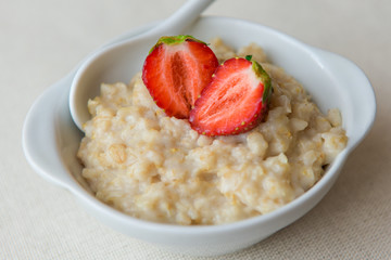 Oatmeal with strawberries in a white bowl. Healthy breakfast with oatmeal and fresh organic berries. Hot and healthy breakfast. Dietary nutrition. Top view, close up