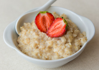 
Oatmeal with strawberries in a white ceramic plate with a spoon. Useful work. Strawberry on oatmeal. Close-up