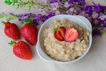 Homemade oatmeal with strawberries in a white plate. Healthy breakfast. Oatmeal with sliced ​​strawberries.