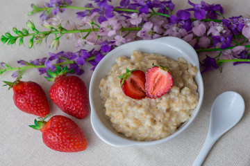 Oatmeal with strawberries in a white bowl. Healthy breakfast with oatmeal and fresh organic berries. Hot and healthy breakfast. Dietary nutrition. Top view, close up