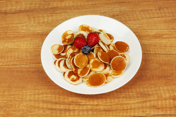 Delicious mini pancakes with blueberries and strawberries lie in a plate on a wooden table. Brunch, Breakfast for children, trendy food