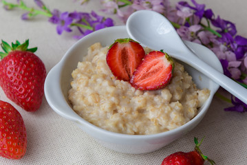 
Oatmeal with strawberries in a white ceramic plate with a spoon. Useful work. Strawberry on...