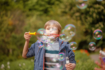 Little cute boy inflates soap bubbles in the park in nature, joyful emotions in a child, bright big...