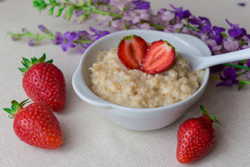 Homemade oatmeal with strawberries in a white plate. Healthy breakfast. Oatmeal with sliced ​​strawberries.