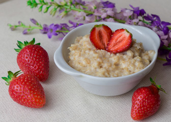 Oatmeal with strawberries in a white bowl. Healthy breakfast with oatmeal and fresh organic berries. Hot and healthy breakfast. Dietary nutrition. Top view, close up
