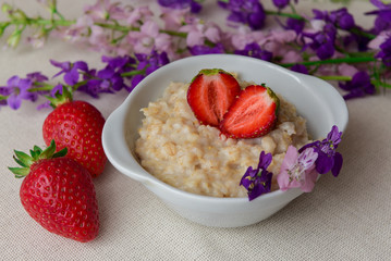 Oatmeal with strawberries in a white bowl. Healthy breakfast with oatmeal and fresh organic berries. Hot and healthy breakfast. Dietary nutrition. Top view, close up
