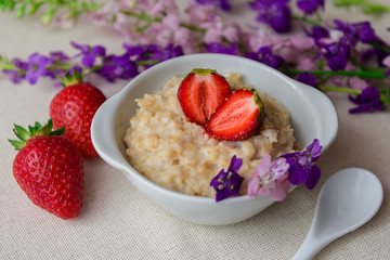 Homemade oatmeal with strawberries in a white plate. Healthy breakfast. Oatmeal with sliced ​​strawberries.