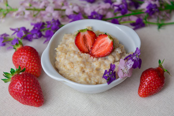 Oatmeal with strawberries in a white bowl. Healthy breakfast with oatmeal and fresh organic berries. Hot and healthy breakfast. Dietary nutrition. Top view, close up