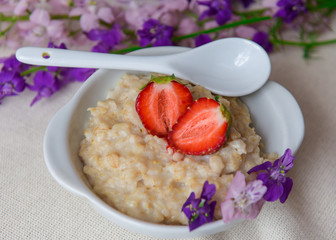
Oatmeal with strawberries in a white ceramic plate with a spoon. Useful work. Strawberry on oatmeal. Close-up