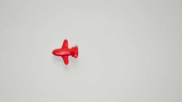 Stop motion animation of the red plastic toy plane flying on a white paper.
