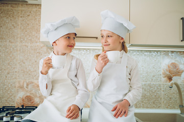 kids cooks in modern kitchen in white bathrobes and hats