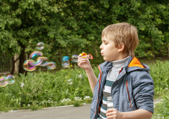 Little cute boy inflates soap bubbles in the park in nature, joyful emotions in a child, bright big...