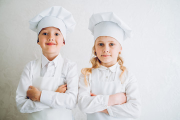 kids cooks in modern kitchen in white bathrobes and hats