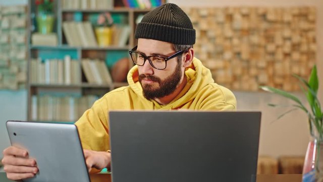 Young looking guy with a smart glasses working online from home he using the electronic tablet and laptop at the same time to finish his work