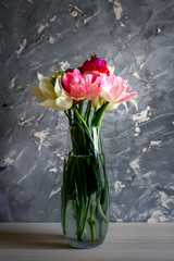 A glass vase filled with a bouquet of bright tulips stands on dark background.
