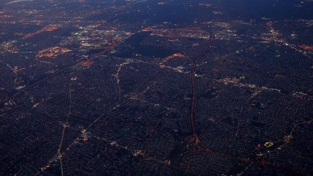 Aerial view of American East Coast seen from airplane flying to NY in the sky at sunset. Jet landing on city landscape with roads, homes, lights. Urban sprawl in United States of America, USA