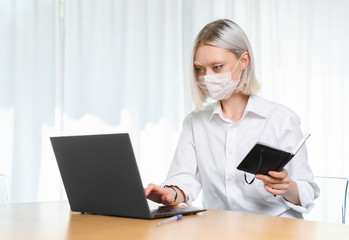 
A young girl works with a laptop at home or in the office. antiviral mask.