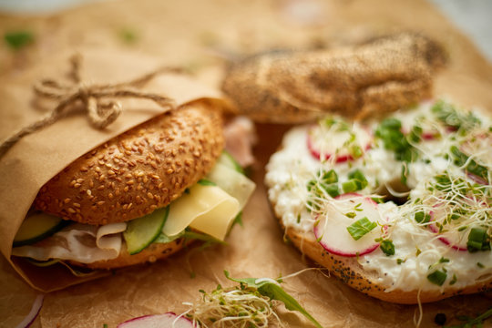 Bagels with ham, cream cheese, hummus, radish wrapped in brown baking paper ready for take away