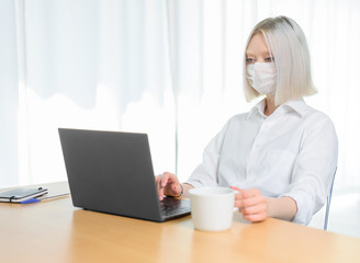 
A young girl works with a laptop at home or in the office. antiviral mask.