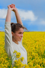 Naklejka na ściany i meble Brunette girl in rapeseed field summer time, facing side way blue sky background. Happy beautiful young woman on blooming rapeseed field full of joy and happiness. Concept of freedom and childhood