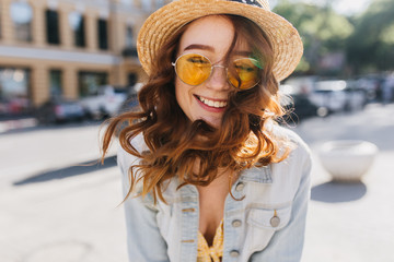 Gorgeous dark-haired lady in denim jacket having fun in summer weekend. Outdoor portrait of excited ginger girl in sunglasses expressing happy emotions.