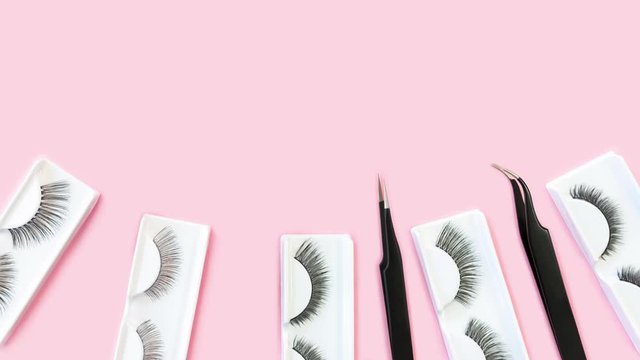 Different tools for eye lash extension on trendy pastel pink background. Fake eyelashes and tweezers. Beauty concept. Makeup cosmetics. Top view, flat lay. Place for text. Banner. Stop motion.