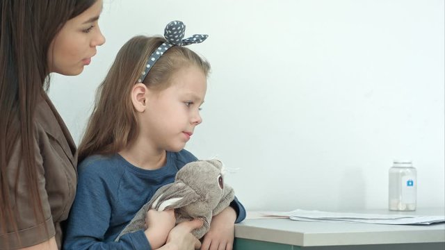 Mother Holding Little Girl And Taking Her Temperature With Thermometer At Doctor Office