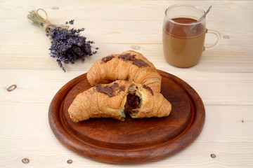 croissants with chocolate and a cup of coffee with milk on a wooden table