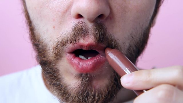 bearded guy man paints his lips with brown lipstick