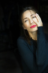 Young woman with red lipstick on a dark background. A woman touches her face with her hand.