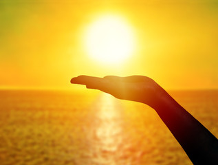 Woman hand holding sun at sunset on the beach