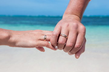 Bride and groom exchanging wedding rings close up during symbolic nautical decor destination wedding marriage on sandy beach in front of the ocean in Punta Cana, Dominican republic 