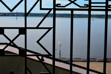 pattern of an iron forged fence against the background of the river of the city embankment