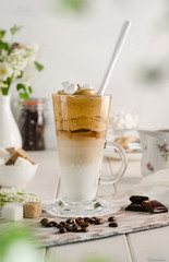 Obraz na płótnie Canvas Cold coffee dalgon in a tall glass on a white wooden background. Foam whipped with a mixer made of sugar, instant coffee and water in cold milk with ice. Korean and indian whipped coffee.