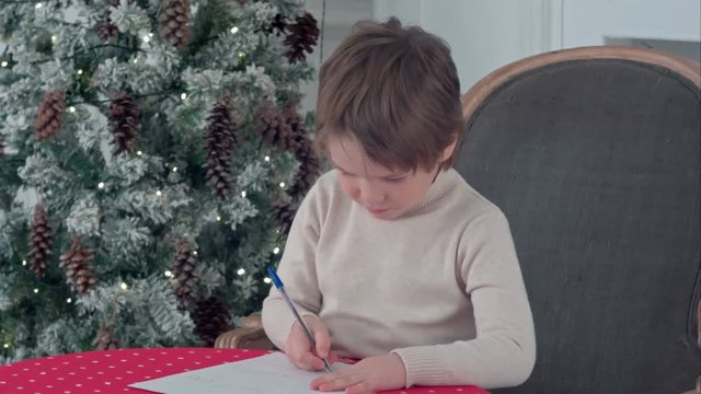 Concentrated little boy writing letter to Santa Claus at table