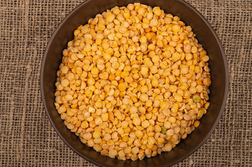 Yellow split peas in a ceramic bowl on a background of coarse-textured burlap. Traditional cereals for making soups and porridge. Close up.