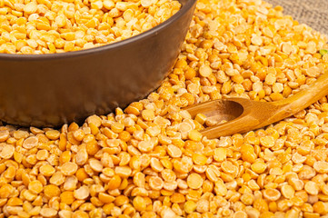 Yellow split peas in a ceramic bowl and grits scattered on a background of coarse-textured burlap. Traditional cereals for making soups and porridge. Close up.