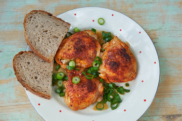 Top view on roasted hot spicy chicken leg pieces sprinkled with chopped spring onion and two slices of rustic bread. Served on the vintage porcelain plate. Tasty and juicy delicious light dietary dish