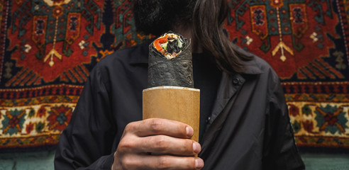Shawarma doner roll in black pita in man hands