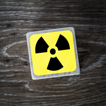A yellow radiation or radioactive warning symbol, sign or icon on a wooden background