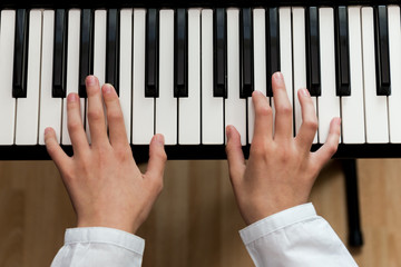 a schoolgirl in a white shirt plays the keys of a synthesizer. selective focus